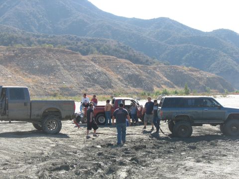 1987 Ford Bronco - Group of people and off-road vehicles in a remote, dry riverbed area.