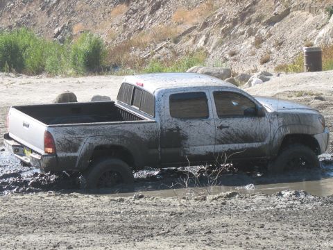 1987 Ford Bronco - A silver pickup truck is stuck in a muddy area, with its tires submerged.