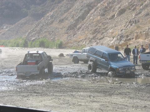 1987 Ford Bronco - Off-road vehicles navigating a muddy terrain with a steep hillside.