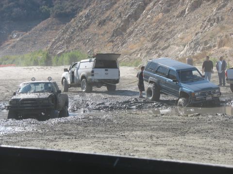 1987 Ford Bronco - Several off-road vehicles are stuck in a muddy terrain, with one vehicle attempting to pull another out.