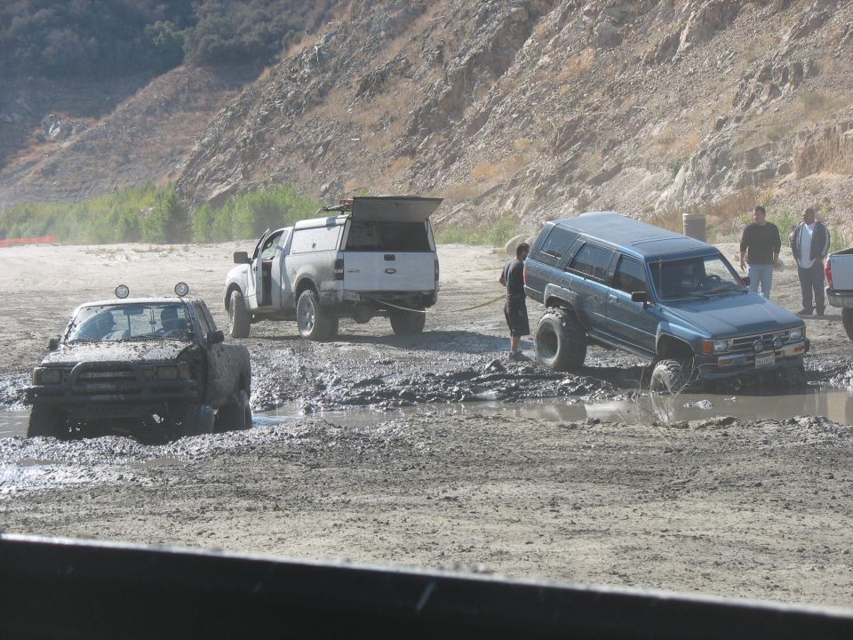 Muddy off-road vehicles stuck in a muddy area. One truck is being pulled by another