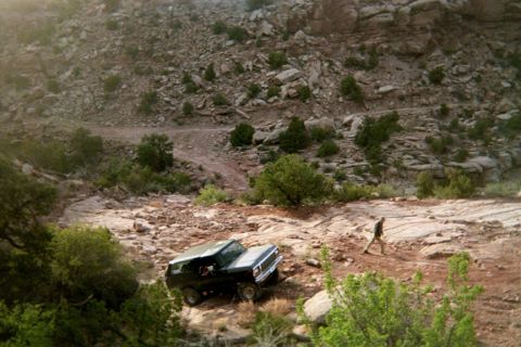 1979 Ford Bronco - A dark SUV navigates a , rocky terrain, with a lone figure walking in the distance. The vehicle resembles a 1978 Ford Bronco.