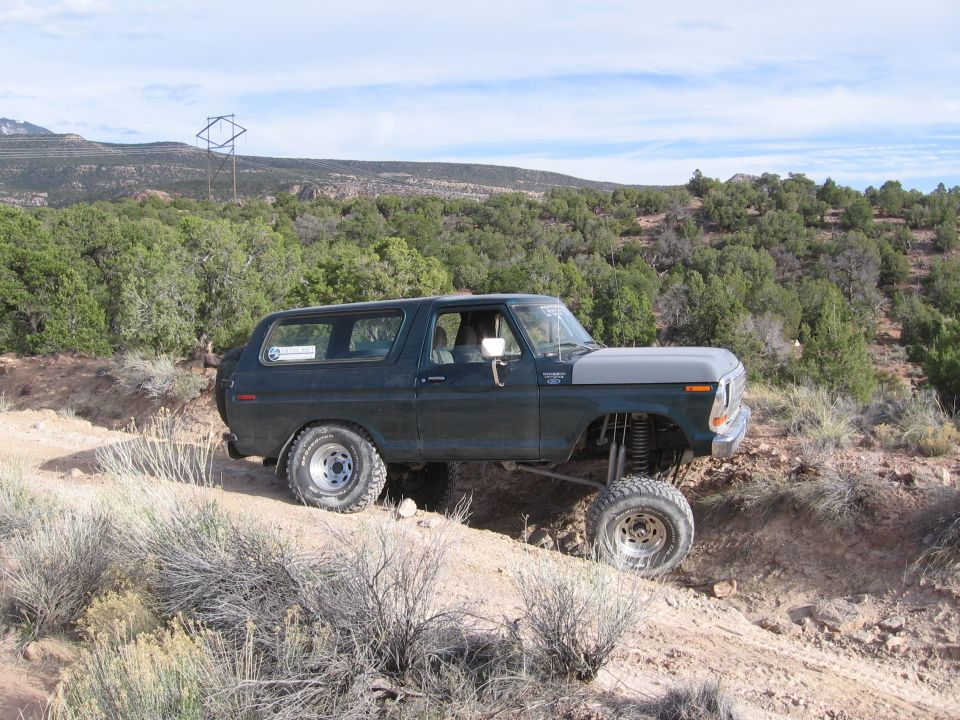 Dark green lifted Ford Bronco flexing on a rutted desert trail, passenger side