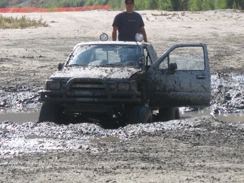 1987 Ford Bronco - This mud-covered pickup truck appears to be stuck in a muddy off-road area, with the driver's side door wide open.