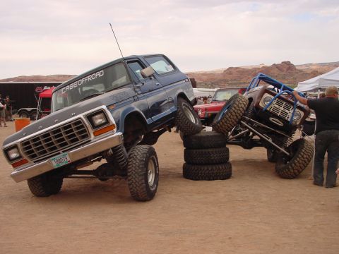1979 Ford Bronco - Two heavily modified Ford Broncos are positioned on a dirt course, one atop a stack of tires.