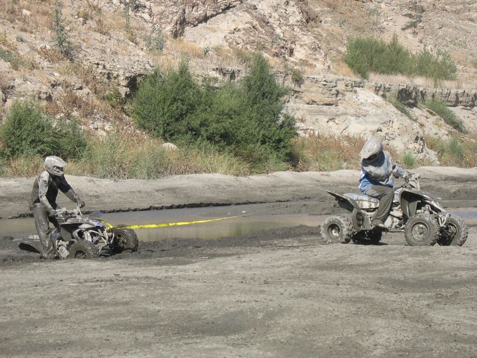 One ATV stuck in mud, another ATV pulling it with a yellow strap
