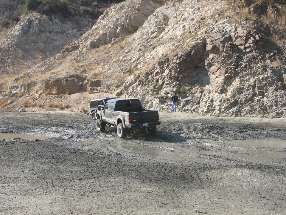 Black pickup truck driving through mud, another vehicle behind it