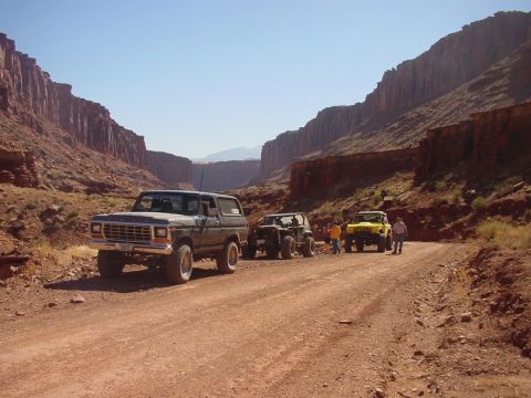 1979 Ford Bronco - A convoy of off-road vehicles travels through a scenic canyon under a clear blue sky.