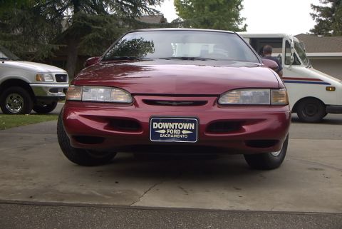 1995 Ford Thunderbird - A red sedan is parked on a driveway, with a white truck visible behind it.