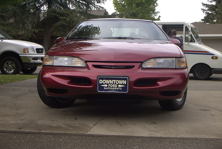 Red sedan with a 'Downtown Ford Sacramento' plate. White truck in background