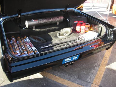 1998 Ford Crown Victoria - Open trunk of a black custom car showing a chrome air tank, subwoofer, amplifiers, and Mothers detailing products.