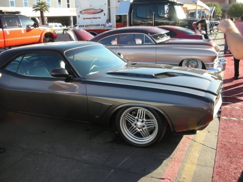 1998 Ford Crown Victoria - gray Dodge Challenger custom with a hood scoop and chrome wheels parked next to a maroon lead-sled on a red show surface.