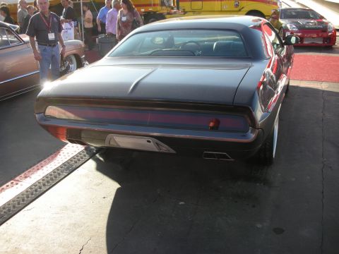 1998 Ford Crown Victoria - Rear view of a dark custom Plymouth Barracuda showing its full-width taillight panel, parked on a red show carpet.