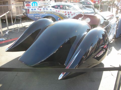 1998 Ford Crown Victoria - Rear view of a black custom streamliner show car with finned teardrop fenders, roped off near a flame-graphic display car.