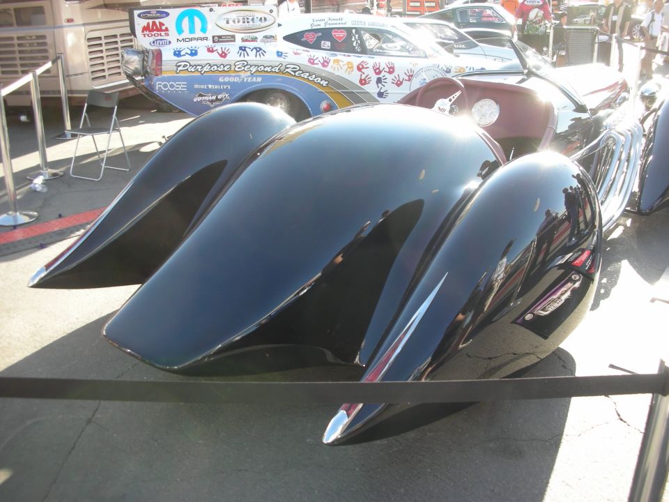 Rear of black custom streamliner with finned teardrop fenders behind show ropes