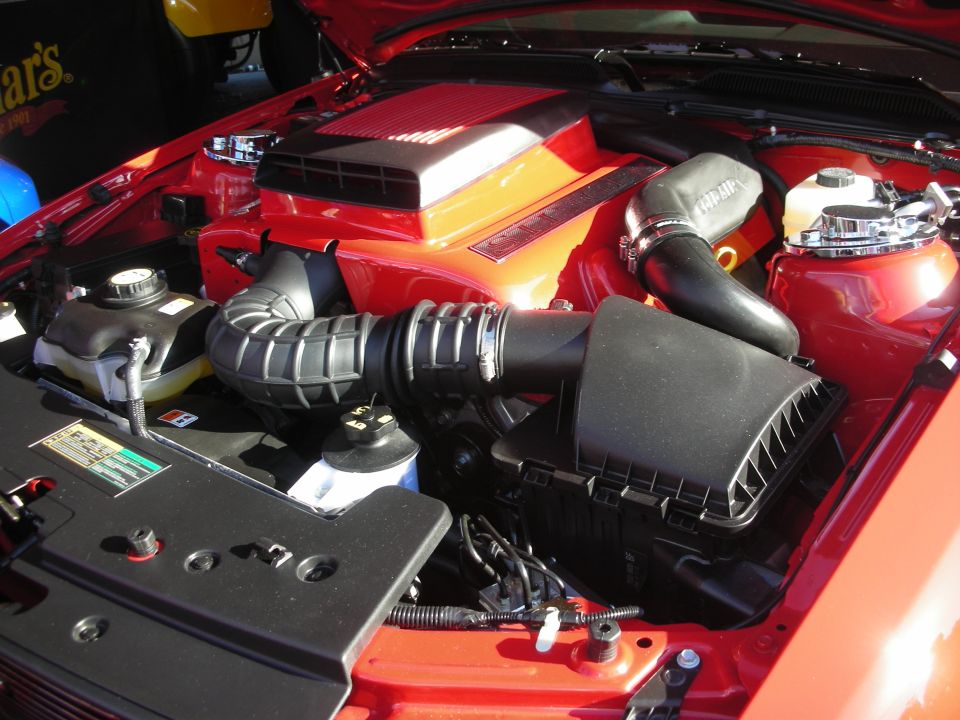 Engine bay of a red car showing black air intake and orange engine cover