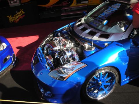 1998 Ford Crown Victoria - bright blue show car displays a heavily chromed supercharged engine under its open hood on a red carpet.