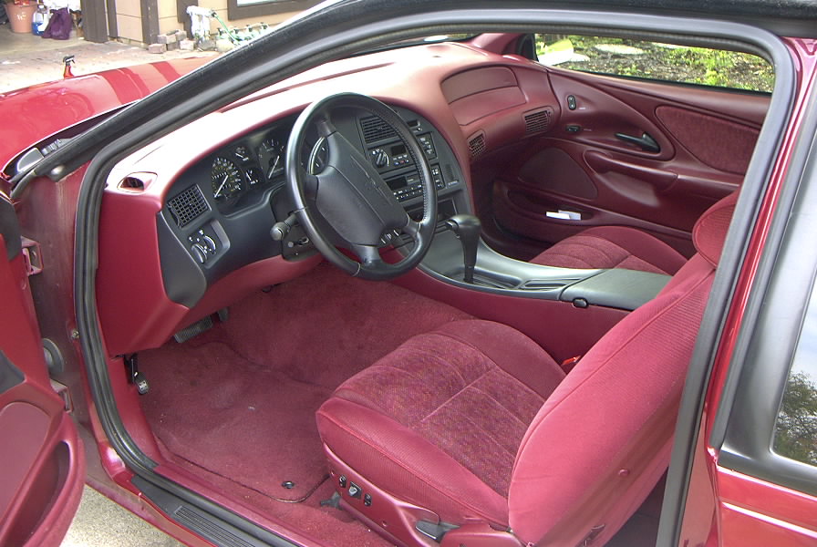 Red and gray coupe interior with cloth bucket seats, dash and steering wheel
