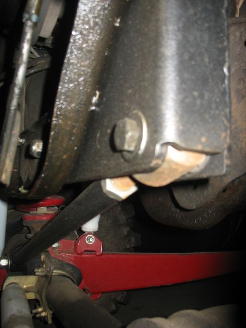 1987 Ford Bronco - Undercarriage view of suspension parts, including a red sway bar bracket and black metal components.