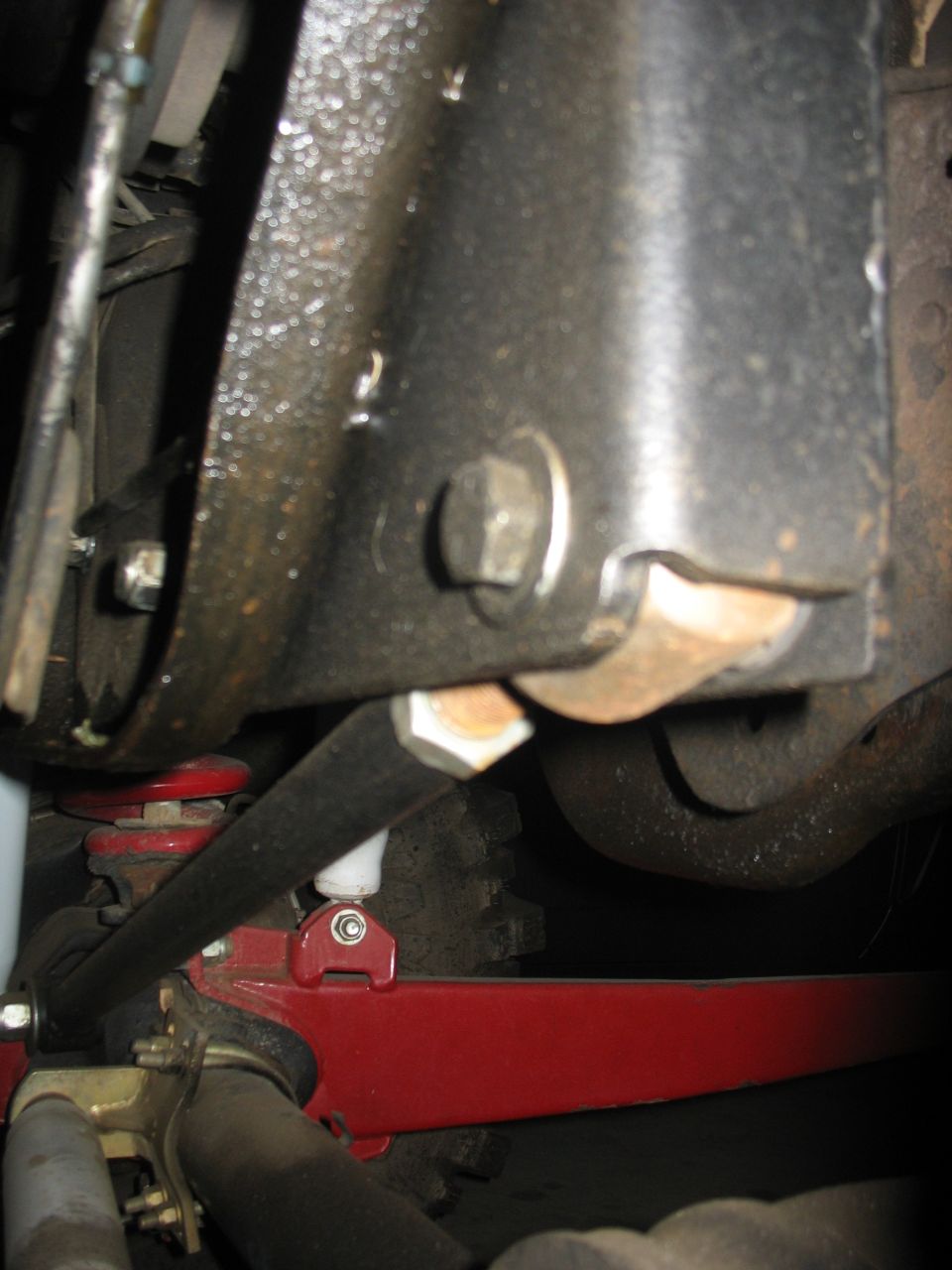 Underbody close-up of frame mount, black radius arm and red suspension brackets on lifted truck