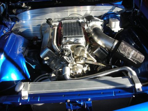 1998 Ford Crown Victoria - polished aluminum supercharged engine with a metal intake pipe fills the engine bay of a blue car.