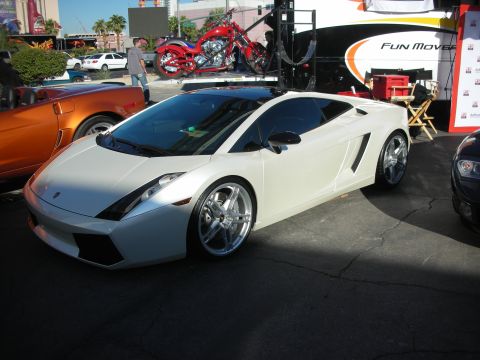 1998 Ford Crown Victoria - white Lamborghini Gallardo with chrome wheels is parked on asphalt with vehicles and a tent in the background.
