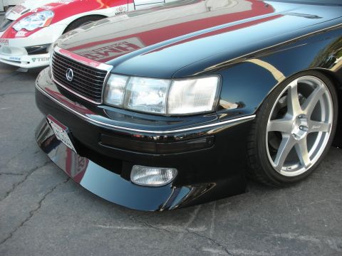 1998 Ford Crown Victoria - close-up of the front corner of a black Lexus sedan showing the headlight, fog light and silver wheel.