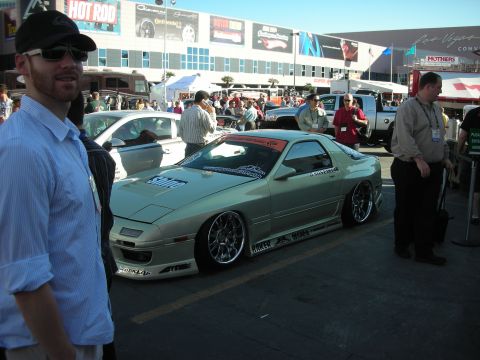 1998 Ford Crown Victoria - low tan widebody sports car with chrome wheels sits among crowds outside a convention center.