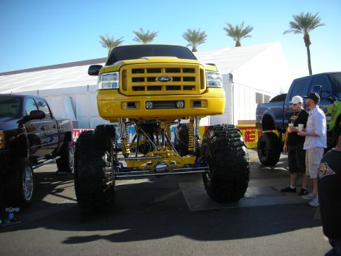 1998 Ford Crown Victoria - yellow Ford Super Duty truck is raised high on a long-travel suspension and massive tires at an outdoor show.