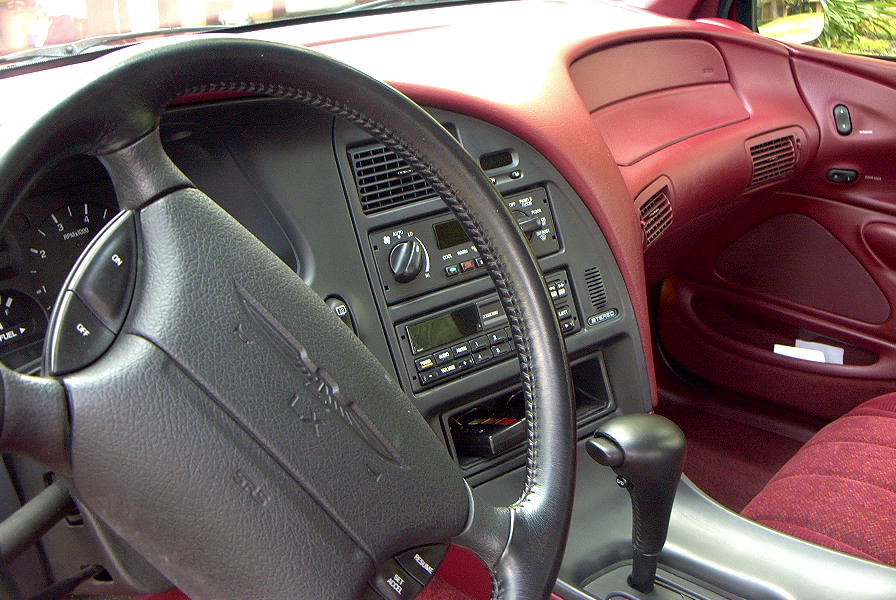 Car interior with black steering wheel, dash controls, and maroon upholstery
