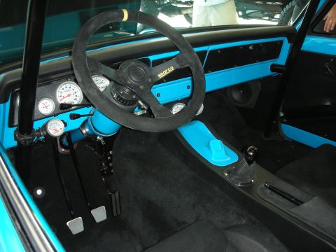 1998 Ford Crown Victoria - Race-built interior with a suede Sparco steering wheel, gauge cluster, shifter, and bright turquoise trim against black carpet.
