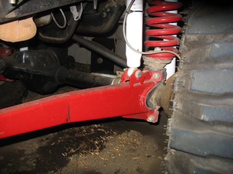 1987 Ford Bronco - Close-up view of off-road suspension components, including a red control arm and coil spring.