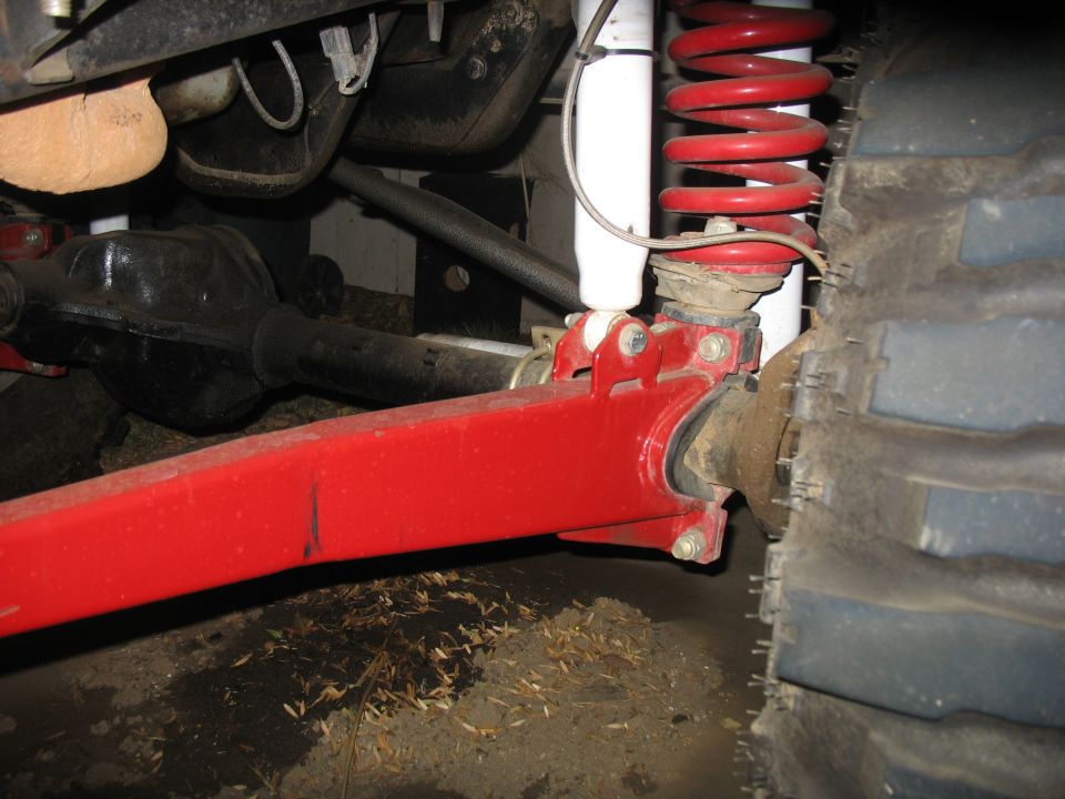 Red radius arm and red coil spring over white shock on a lifted 4x4 front axle, underbody view