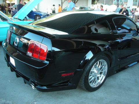 1998 Ford Crown Victoria - Glossy black late-model Ford Mustang coupe with a body kit and polished chrome wheels at an outdoor show.