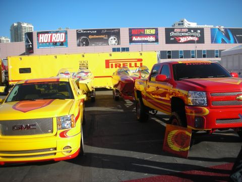 1998 Ford Crown Victoria - Yellow GMC and red pickups with matching trailers on a Pirelli display, beneath Hot Rod and Motor Trend banners.