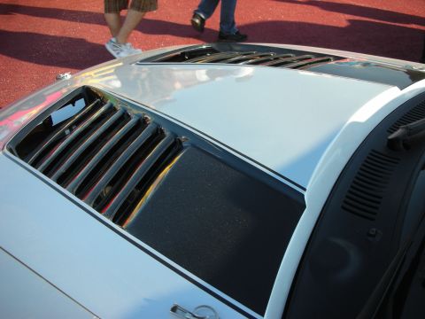 1998 Ford Crown Victoria - Detail of a silver car's louvered rear window and decklid, photographed from above on a red show surface.