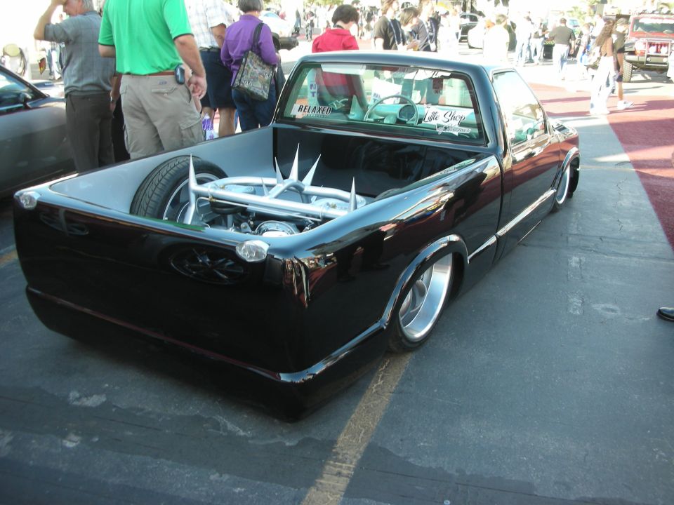 Lowered black-and-white mini pickup with chromed engine in the bed at a show