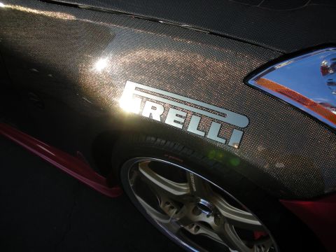 1998 Ford Crown Victoria - Close-up of a carbon-fiber front fender bearing a polished PIRELLI emblem above a gold five-spoke wheel.