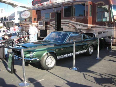 1998 Ford Crown Victoria - dark green Shelby GT500 fastback Mustang with white side stripes sits roped off in front of a motorhome at an auction event.