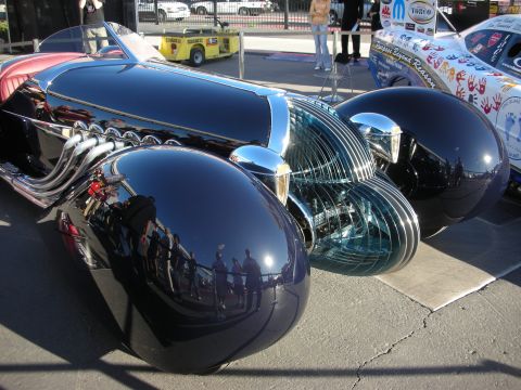 1998 Ford Crown Victoria - Side view of a black streamlined art-deco custom car displaying polished chrome and teal louvered trim panels at an outdoor show.