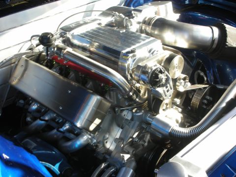 1998 Ford Crown Victoria - Close-up of a polished aluminum supercharged V8 engine with a red valve cover and chromed intake piping in a blue car.