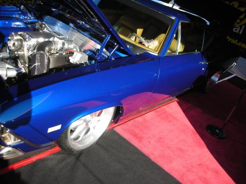 1998 Ford Crown Victoria - deep blue custom coupe sits hood-up on red carpet revealing a polished engine and tan interior at an indoor show.
