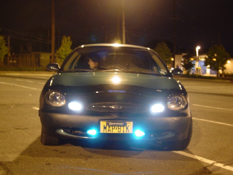 Front view of dark Ford Taurus sedan at night with blue accent lights and headlights on