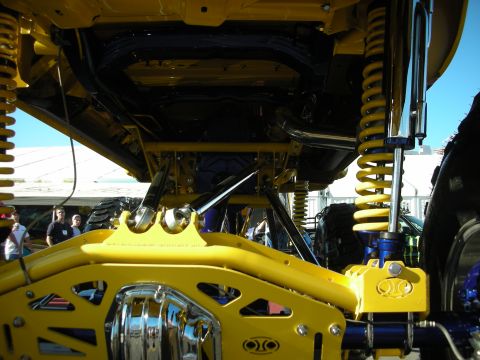 1998 Ford Crown Victoria - Detail of a yellow lifted truck's undercarriage showing painted suspension links, coil-over shocks and a chrome differential.