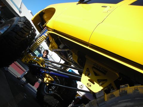 1998 Ford Crown Victoria - Low-angle view of a yellow lifted truck's front suspension with coil-over shocks, blue links and oversized off-road tires.