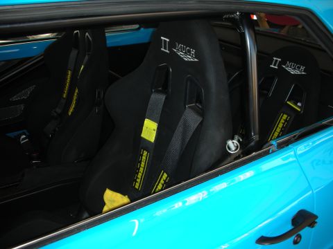 1998 Ford Crown Victoria - Two black racing bucket seats reading II MUCH with Schroth harnesses sit inside a bright turquoise-blue car interior.