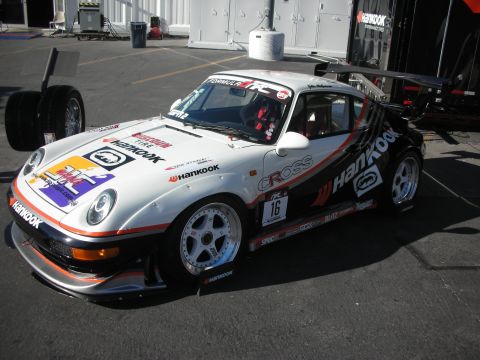 1998 Ford Crown Victoria - white and black Porsche 911 race car wearing Hankook livery and number 16 parked beside service trailers.