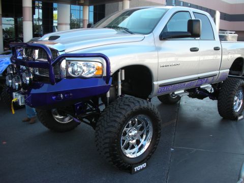 1998 Ford Crown Victoria - silver lifted Dodge Ram crew-cab pickup with a blue brush bumper, auxiliary lights and Toyo tires displayed at a show.