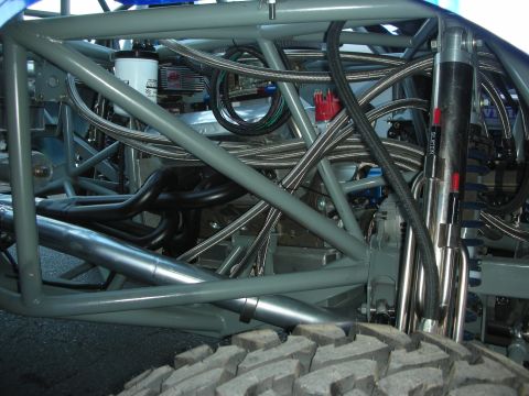 1998 Ford Crown Victoria - Close-up of a gray tube-frame chassis showing exhaust headers, braided steel lines and a coil-over shock above a tire.