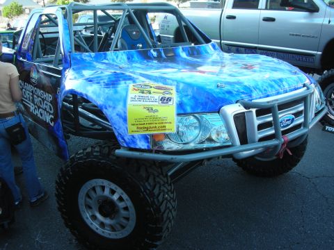 1998 Ford Crown Victoria - blue water-themed off-road race truck with a Ford grille, tube body and prerunner suspension displayed in a show lot.